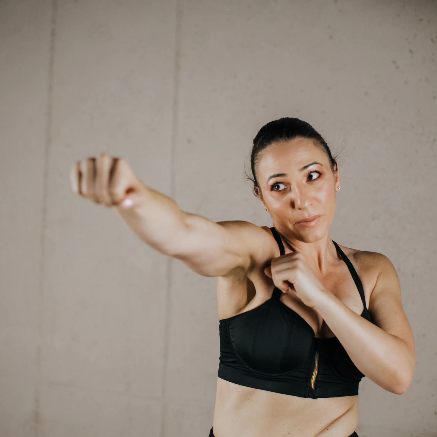 A female model showcasing a black WILDRAX Balconette Sports Bra while demonstrating a boxing stance in a gym